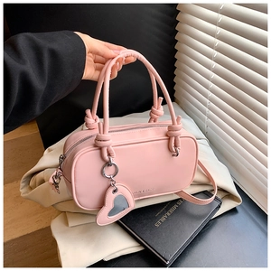 Détail du sac Boston en cuir rose avec poignées à nœuds et breloque miroir en cœur