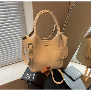 Detail view of cream lychee leather bucket bag with puppy charm and fashion tag