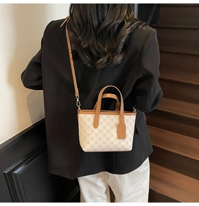 Mannequin portant un sac cabas beige à motifs géométriques marrons sur un blazer noir et pantalon blanc