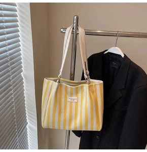Gros plan du sac cabas en toile rayée jaune et blanc avec étiquette de mode en cuir blanc