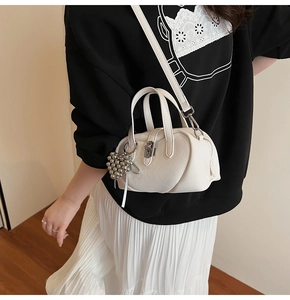 Détail de la texture en cuir blanc et pendentif boule argentée sur le sac bandoulière