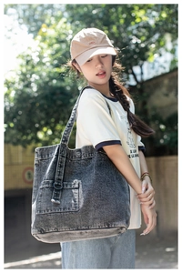 Detail of dark grey washed denim tote bag with metal buckle on a shoulder strap