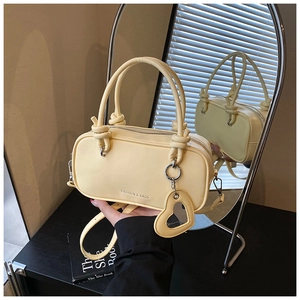 Détail du sac à main jaune avec poignées nouées et breloque miroir en forme de cœur