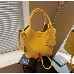 Detail of yellow lychee texture leather bucket bag with dog pendant and fashion plaque
