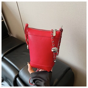 Détail d'un sac seau en cuir rouge avec pendentif tête de mort argenté sur la bandoulière
