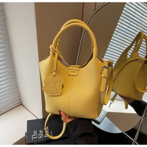 Macro detail of yellow bucket bag featuring pebble leather texture and cute dog charm