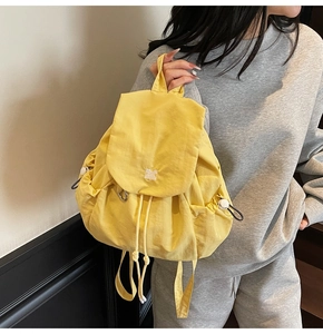 Dettaglio dello zaino in nylon giallo con orsetto ricamato bianco e tasche laterali a coulisse