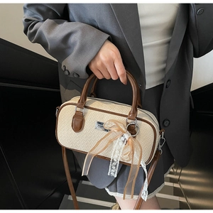 Dettaglio borsa Boston beige a trama coccodrillo con fiocco in pizzo e targhetta in metallo