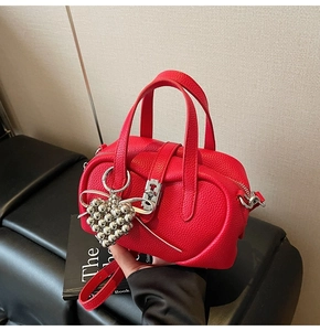 Détail d'un sac Boston rouge grainé avec fermoir rotatif argenté et pendentif en cœur