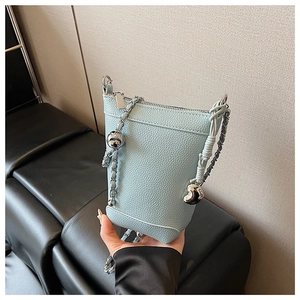 Détail du sac seau bleu clair avec texture litchi, chaîne argentée et breloque coeur