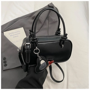 Détail du sac à main en cuir noir avec anse nouée et breloque miroir cœur sur fond de costume