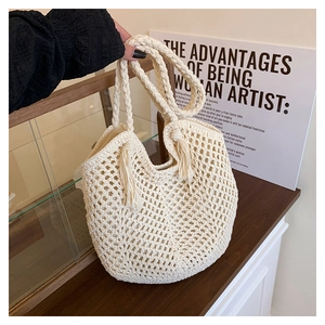 Detail of hollow woven straw tote bag featuring tassel accents and braided handles