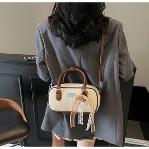 Dettaglio dell'elegante borsa Boston bicolore con fiocco e ciondolo in pizzo su modella