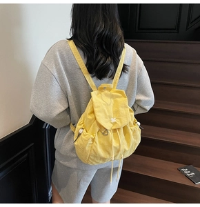 Zaino in nylon giallo con patta a coulisse e tasche laterali indossato da modella
