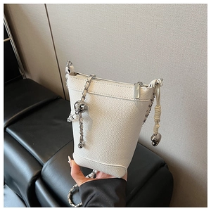 Détail d'un sac seau blanc à motif litchi avec chaîne argentée et breloque cœur
