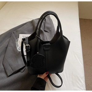Detail of black lychee grain bucket bag with leather puppy charm on white bedding