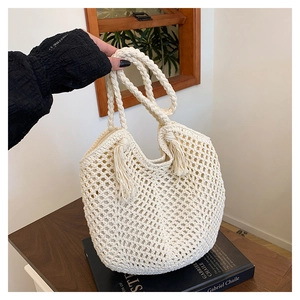 Detail of hollow woven tote bag featuring long tassels and braided handles in cream white