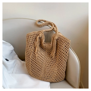 Macro detail of beige hollow out straw tote bag with long tassels on a grey chair