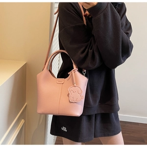 Pink lychee grain leather bucket bag with dog charm and dual handles shown with model