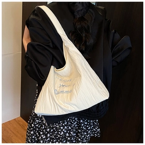 Détail du sac hobo blanc cassé avec broderie bleue et texture plissée porté à l'épaule