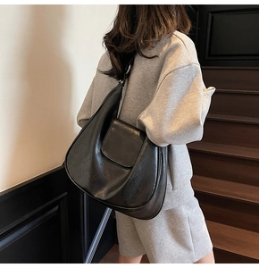 Side view of large matte black crescent bag worn on shoulder in minimalist interior