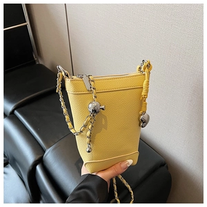Détail du sac seau jaune en cuir grainé avec bandoulière chaîne argentée et breloque cœur