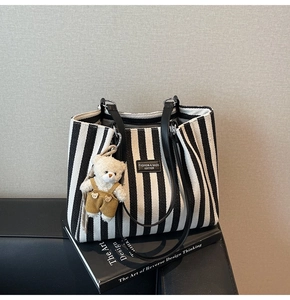 Détail du cabas en toile rayée avec anses en cuir noir et breloque ours en peluche