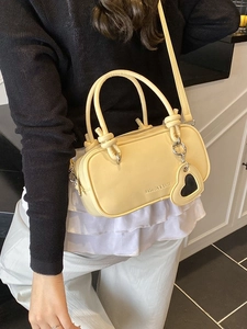 Petit sac à main crème avec poignées nouées et pendentif cœur porté par un mannequin