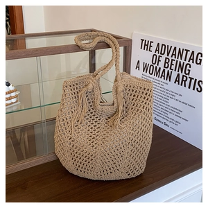 Detail of hollow woven straw tote bag with round braided handle and tassel on wooden stand
