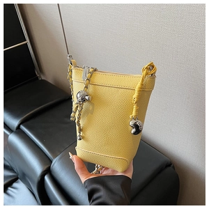 Détail du sac seau jaune avec texture litchi, chaînes argentées et breloques cœur
