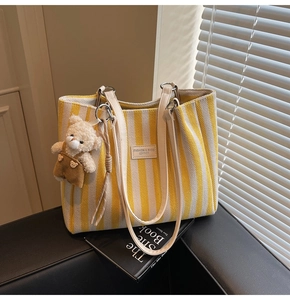 Détail du sac cabas rayé en toile avec poignée en cuir blanc et breloque ours en peluche