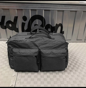 Détail du sac de voyage à carreaux noirs montrant deux poches avant zippées et la texture