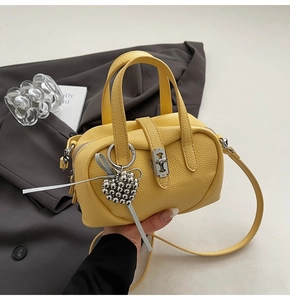 Détail du sac Boston en cuir jaune avec pendentif cœur et fermoir rotatif argenté