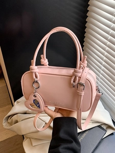 Sac à main rose en cuir avec poignée nouée et breloque miroir cœur sous lumière naturelle