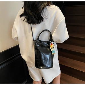 Detail of a shiny black patent leather bucket bag with a cartoon pearl charm on a strap