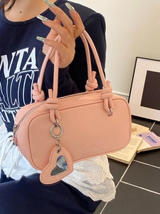 Sac polochon rose en cuir avec poignée à nœud et breloque cœur, vue de trois-quarts