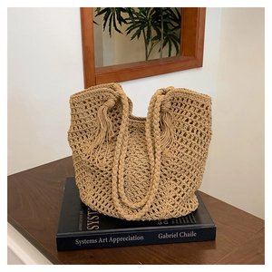 Close-up of beige hollow-out crochet tote bag with fringe tassels on wooden table
