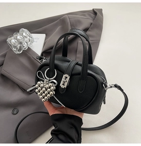 Détail du sac Boston noir en cuir grainé avec un charm en forme de cœur argenté
