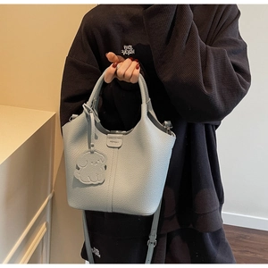 Detailed shot of light blue pebble leather bucket bag with a cute puppy charm and top handle