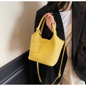 Detail of yellow lychee leather bucket bag with dog charm and adjustable strap
