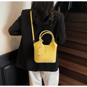 Detail of a bright yellow lychee leather bucket bag with a dog-shaped charm on a model