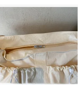 Detail of smooth silver zipper and drawstring toggle on cream nylon dumpling bag
