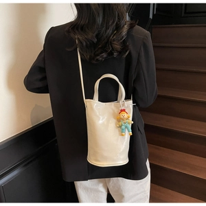 Close-up of a white bucket bag with a cute cartoon doll charm on an indoor staircase