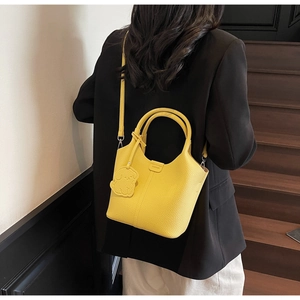 Yellow litchi pattern leather bucket bag with puppy charm shown on a model in a stairwell
