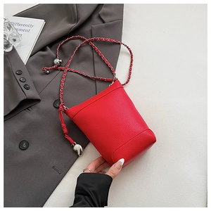 Détail du sac seau rouge à motif litchi avec breloque cœur et bandoulière en chaîne