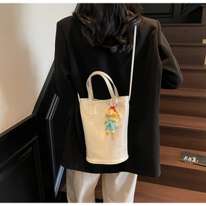 Detailed view of a white patent leather bucket bag with a cute character doll pendant