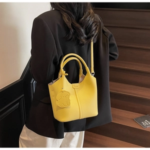 Detail of yellow bucket bag with lychee pattern and cute dog pendant on wooden stairs