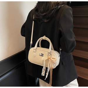 Dettaglio di una borsa Boston beige intrecciata con ciondolo a fiocco e tracolla