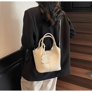Detail view of cream bucket bag with lychee texture and cute puppy charm on shoulder