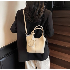 Detail of cream white bucket bag with pebble leather texture and cute dog charm on stairs